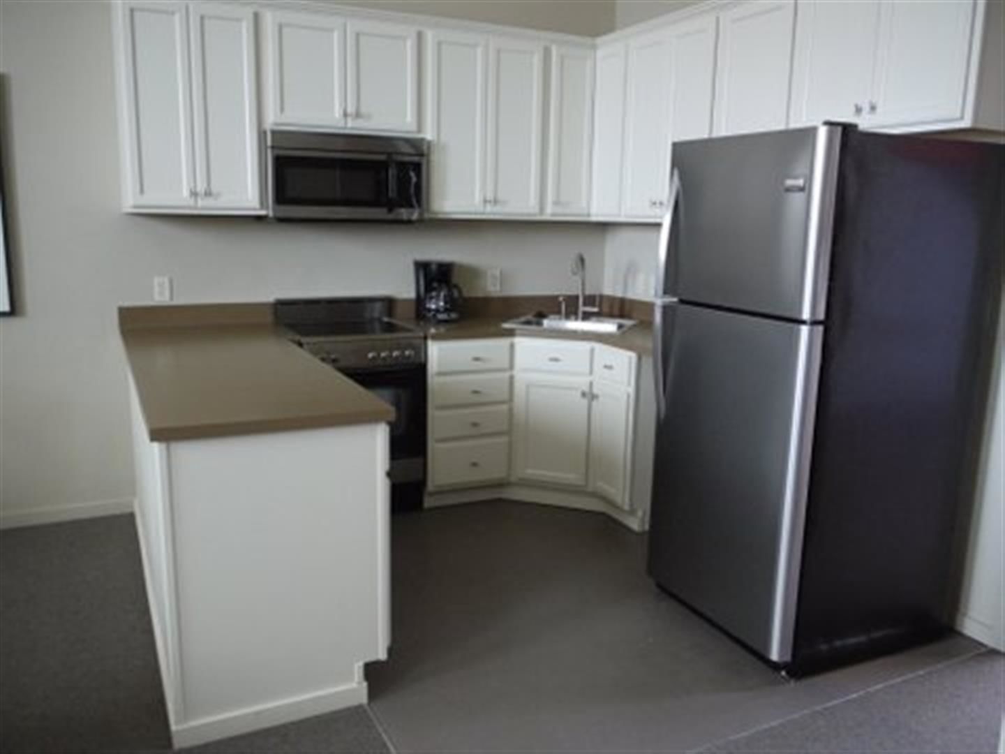 A kitchen with white cabinets, a stainless steel refrigerator, a microwave, and a stove.