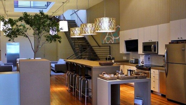A modern kitchen with a central island, bar stools, stainless steel appliances, and a tree in the corner. - The Inn on Whitworth (Brookhaven)