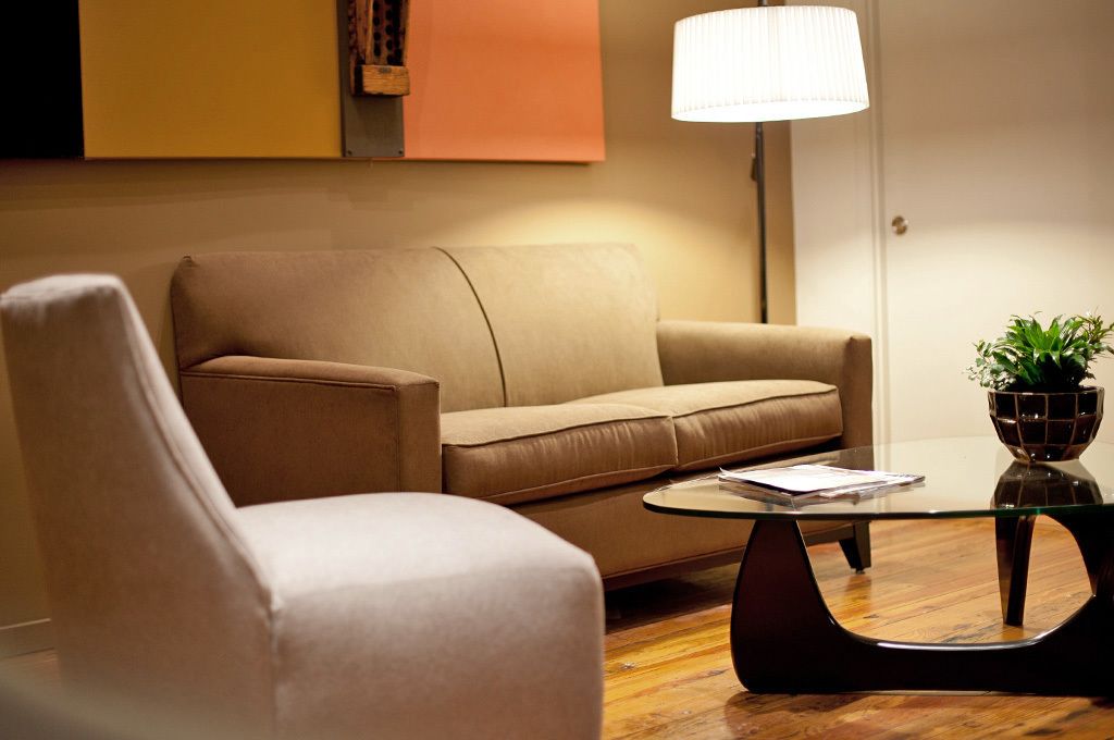 Uma sala de estar moderna com um sofá bege, uma mesa de centro de vidro e um abajur.