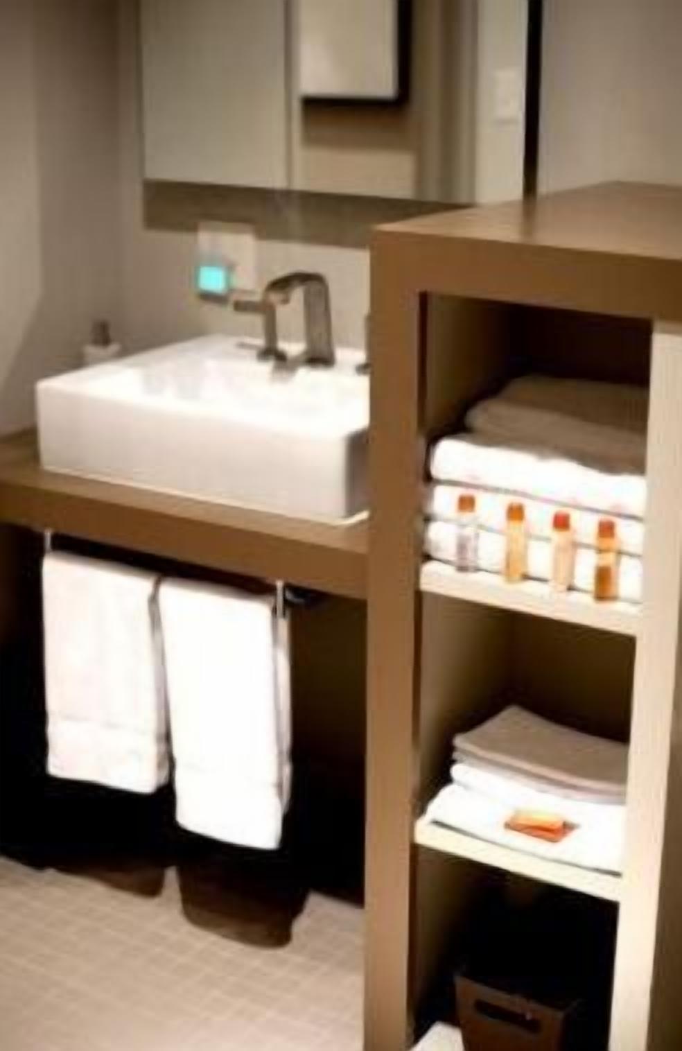 Un baño moderno con un lavabo grande, un espejo y un estante con toallas y artículos de aseo.