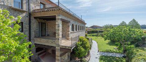 A stone building with a balcony, a garden, and a clear sky.