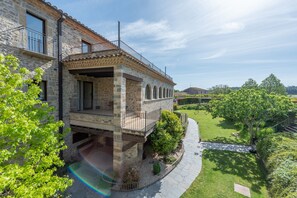 A stone building with a balcony, a garden, and a clear sky. - L'Arcada de Fares (Sant Ferriol)