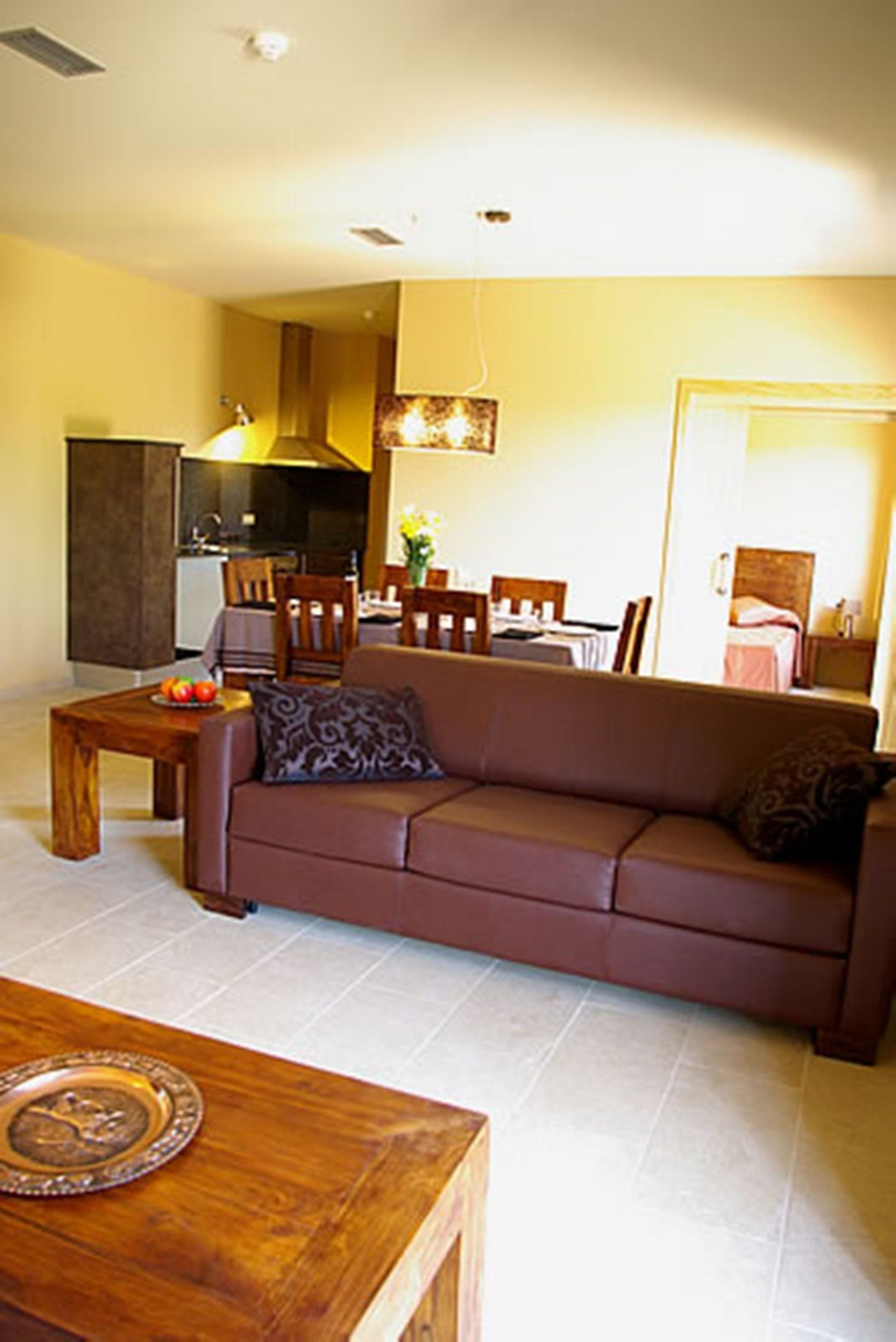 Una sala de estar con un sofá marrón, una mesa de centro de madera y un comedor con mesa y sillas.