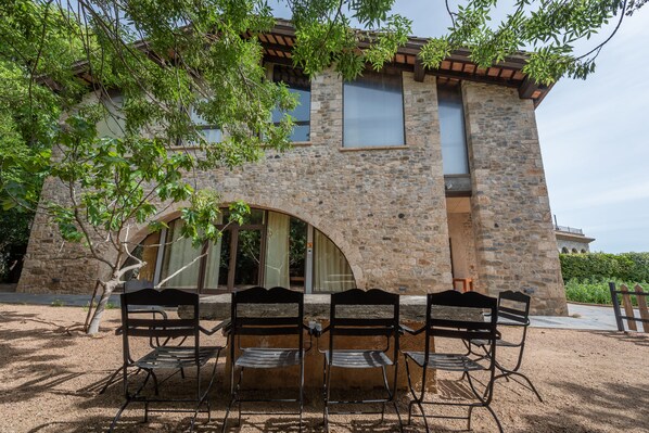 A stone building with a patio area featuring a table and four chairs. - L'Arcada de Fares (Sant Ferriol)