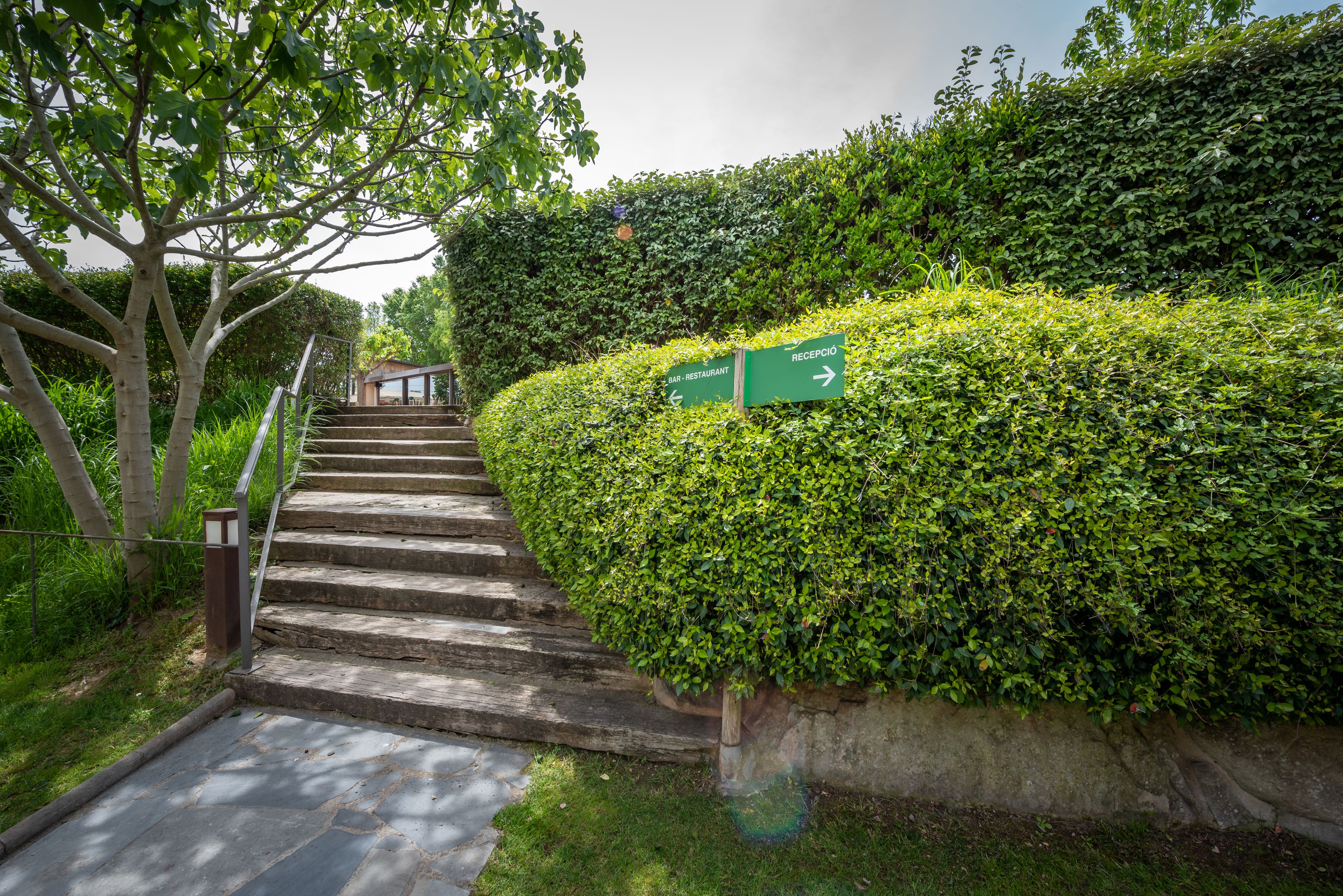 Escadaria conduzindo a um edifício, cercada por vegetação exuberante e uma placa indicando um restaurante.
