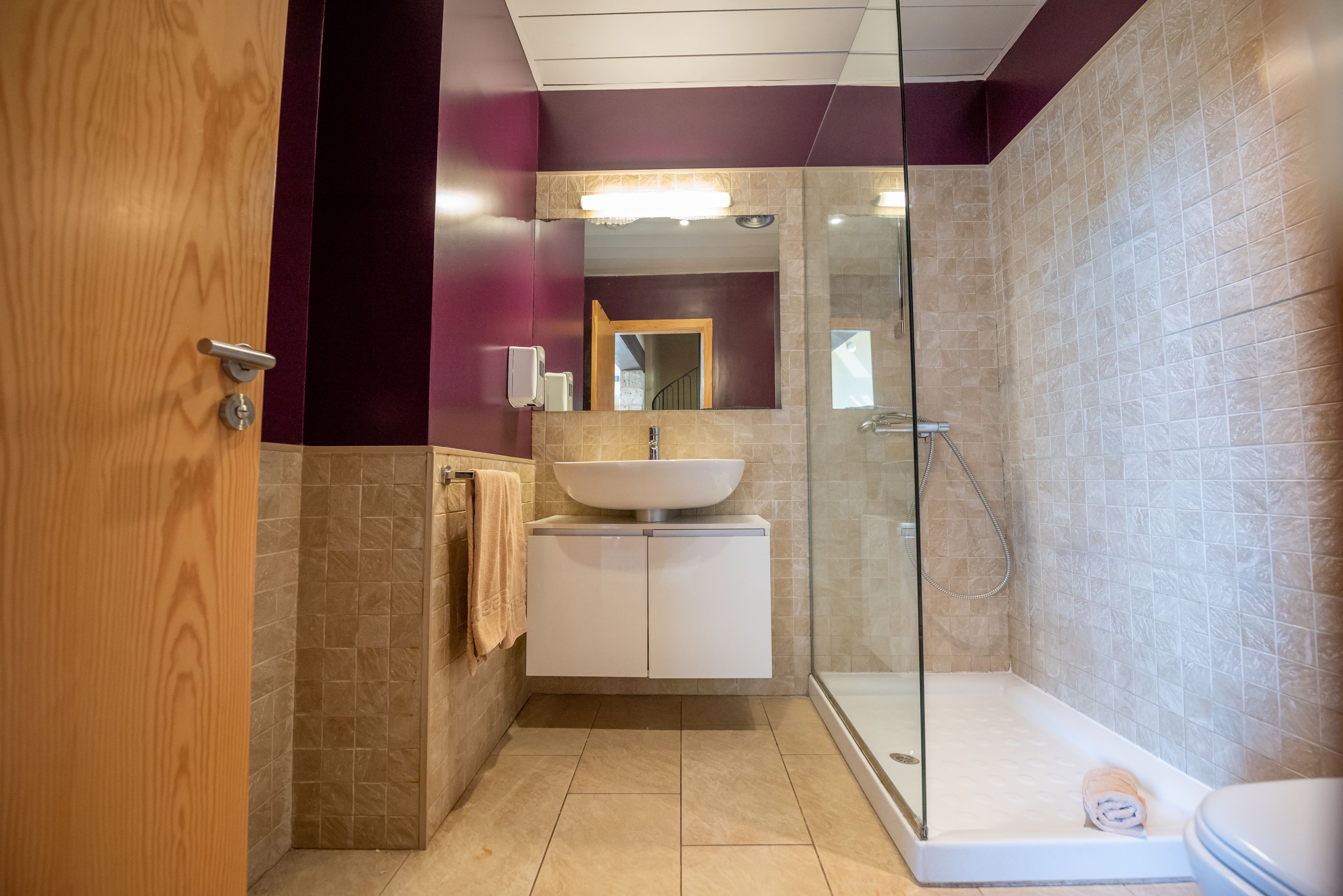Un baño con cabina de ducha de vidrio, un lavabo blanco y una puerta de madera.