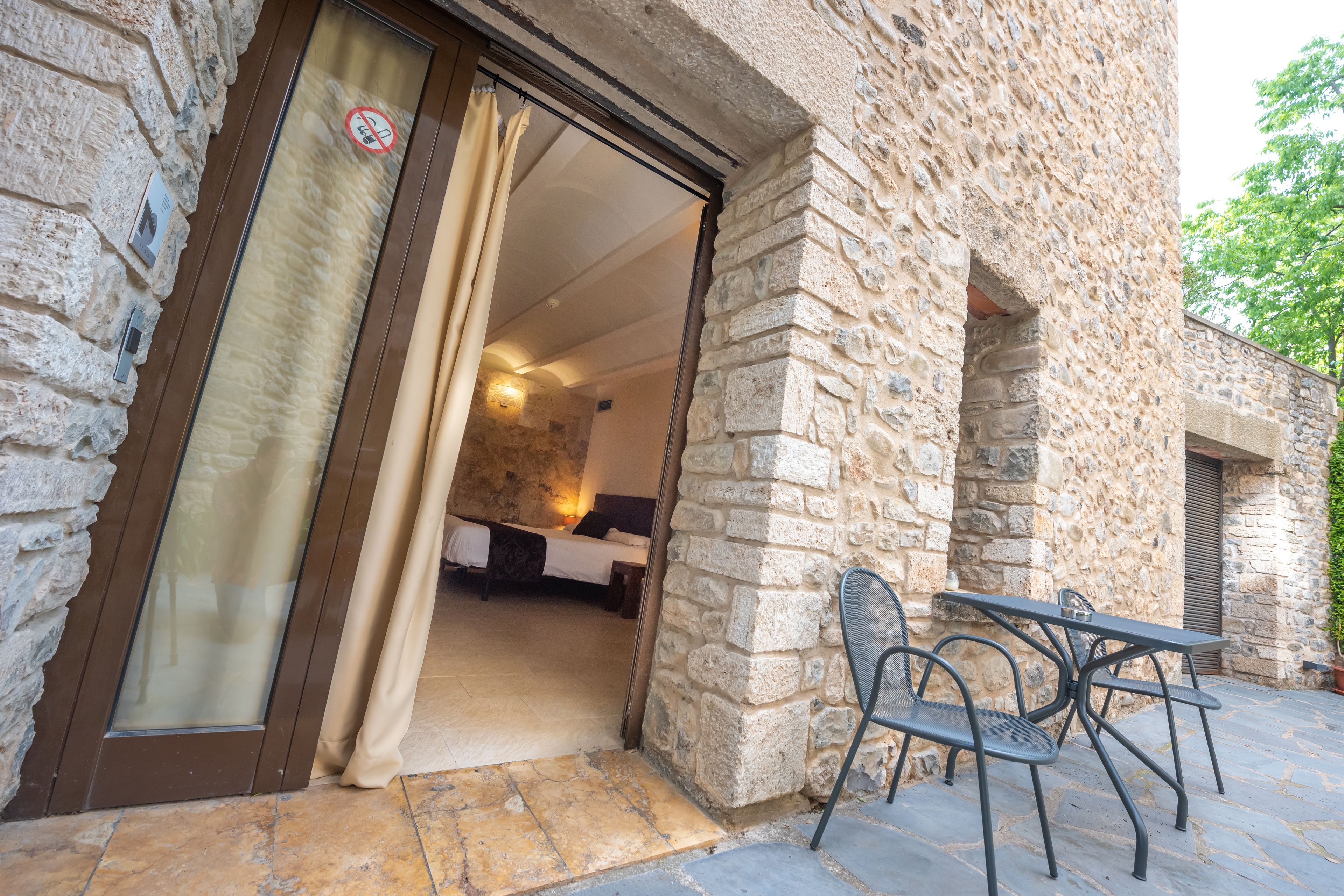 A stone building with a bed and a table with chairs in the entrance area.