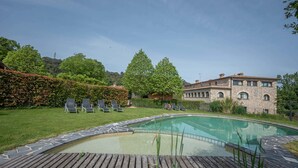 A swimming pool with a wooden deck, lounge chairs, and a stone building in the background. - L'Arcada de Fares (Sant Ferriol)