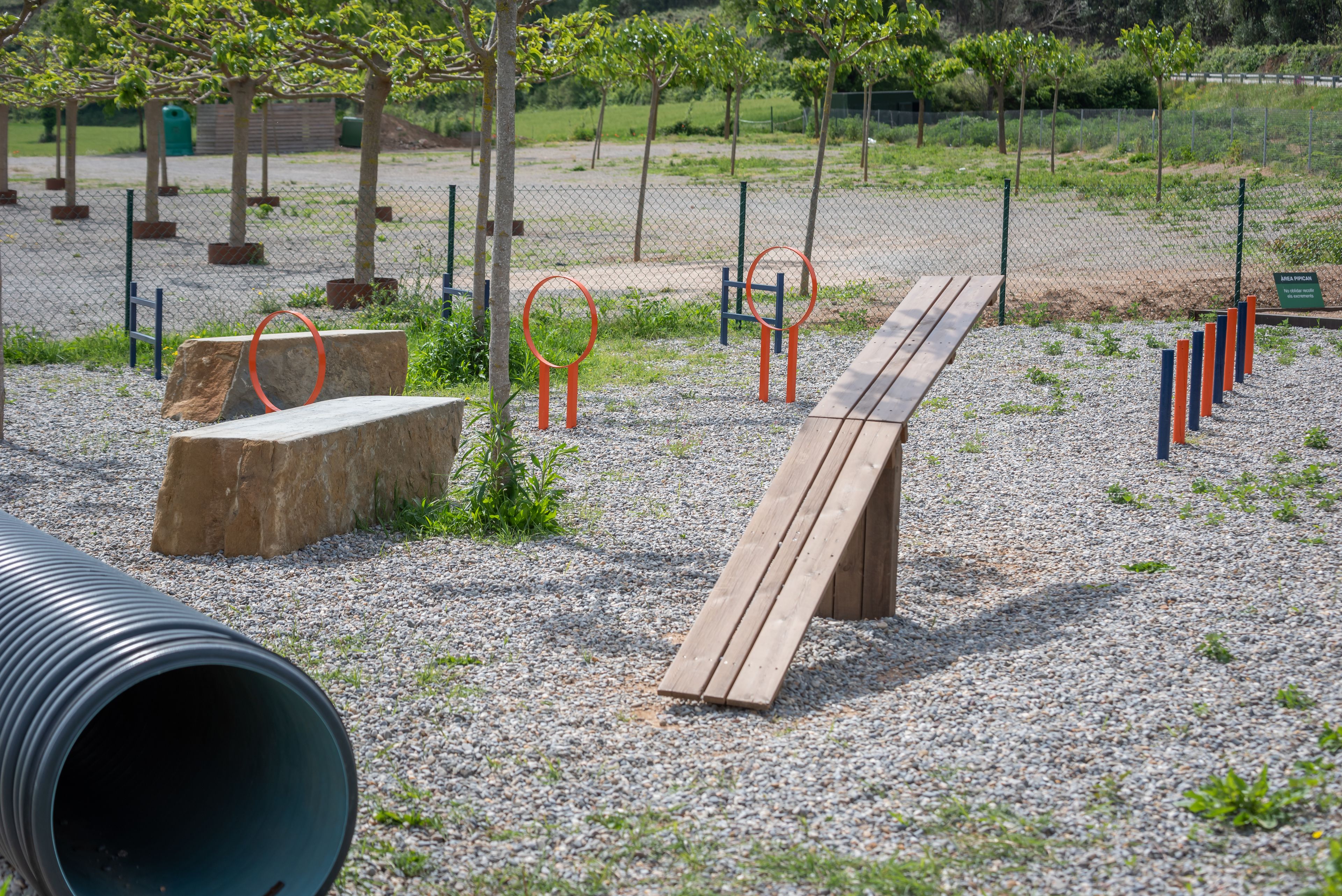 An outdoor exercise area with a wooden bench, exercise rings, and a large pipe.