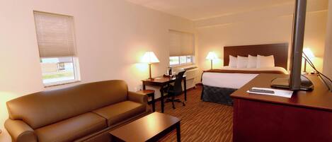 Ein Hotelzimmer mit Bett, Schreibtisch, Sessel, Sofa und Fernseher.