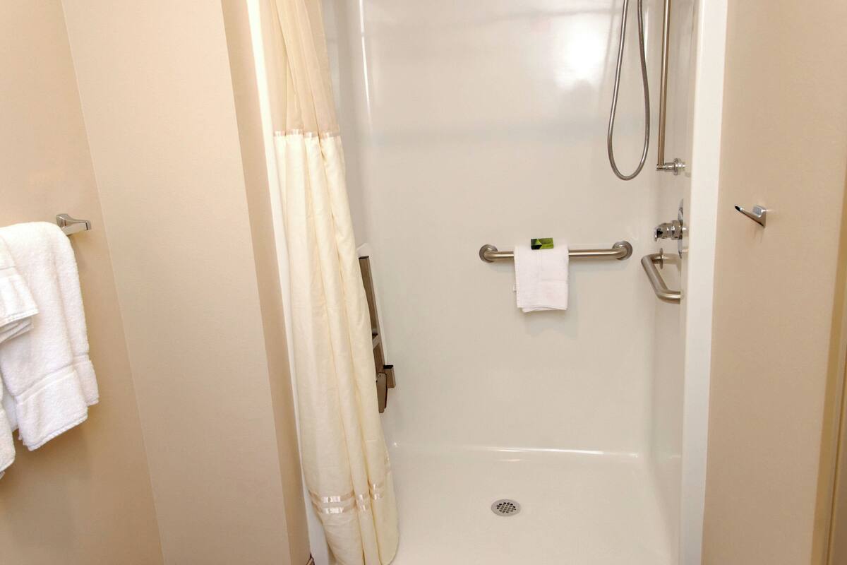 A bathroom with a shower, a towel rack with towels, and a toilet paper holder.
