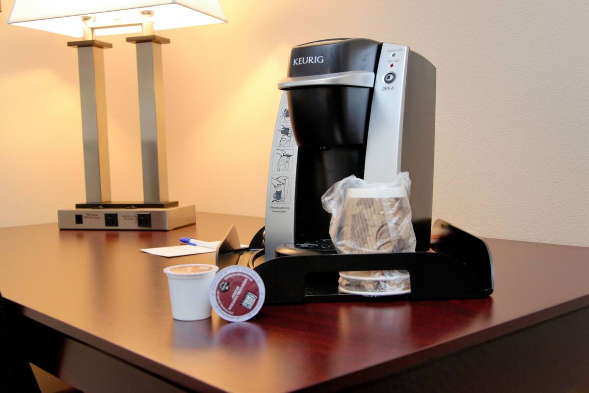 A coffee maker with a cup of coffee and a disposable cup on a table.