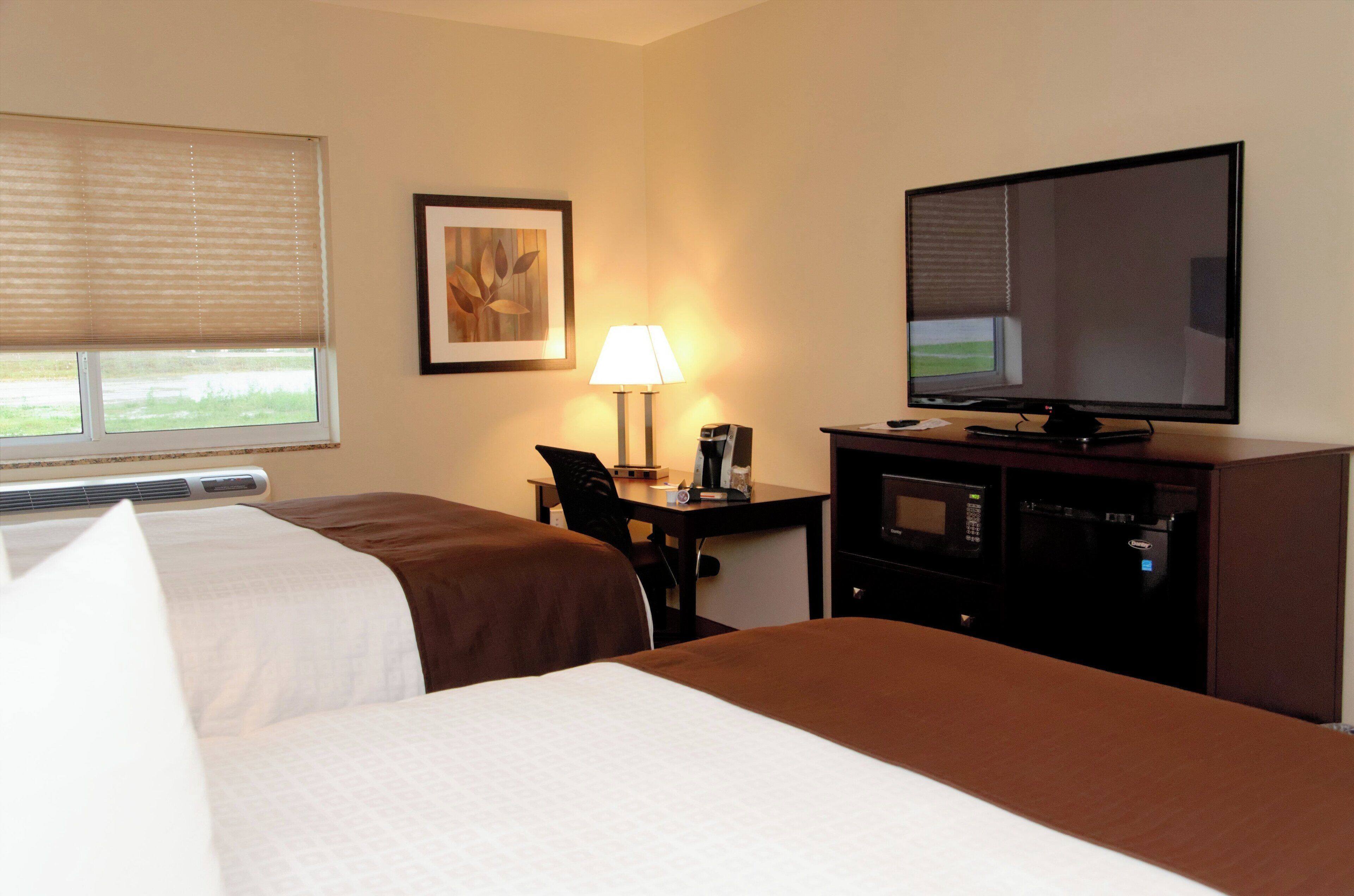 A hotel room with two beds, a desk with a lamp, a television, and a microwave.