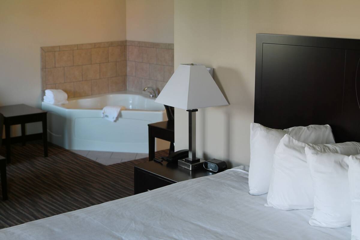 A hotel room with a bed, a sofa, a small table, a lamp, a nightstand, a TV, a bathroom with a bathtub, and two framed pictures on the wall.