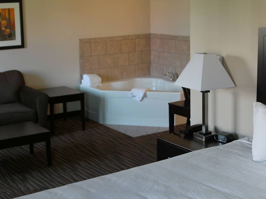 A hotel room with a bed, a sofa, a small table, a lamp, a nightstand, a TV, a bathroom with a bathtub, and two framed pictures on the wall.