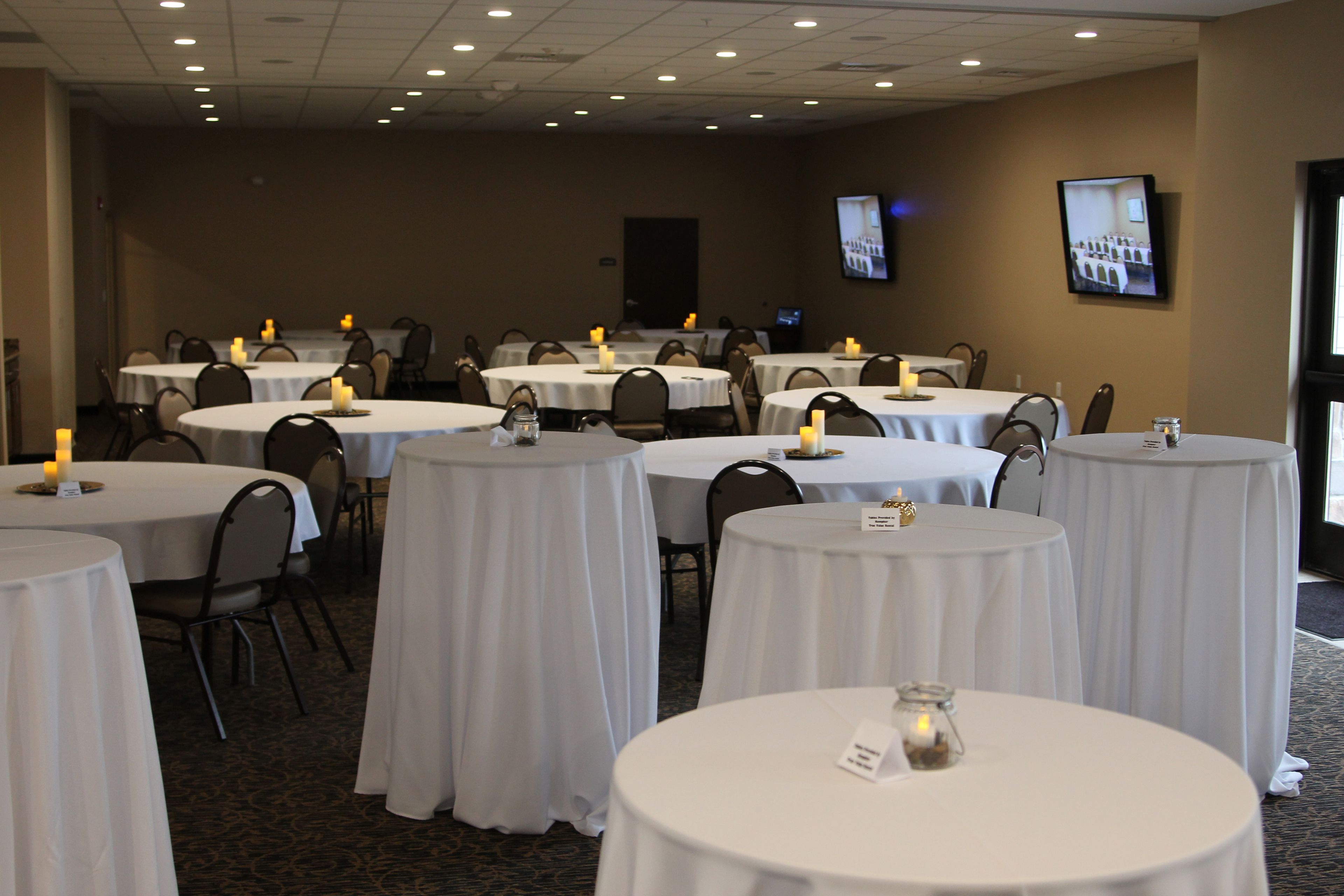 A conference room with multiple round tables, each with a white tablecloth and candles.