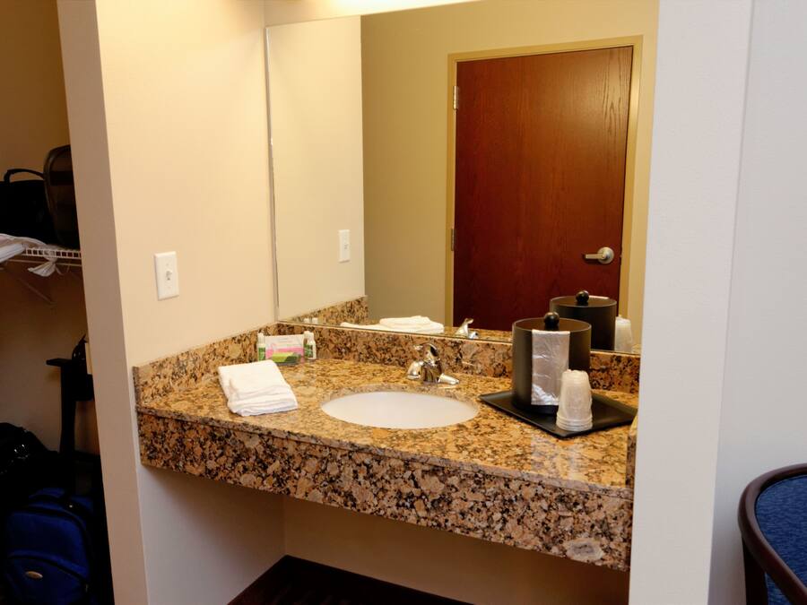 Un bagno d'albergo con lavabo su piano in granito, uno specchio e una porta in legno.