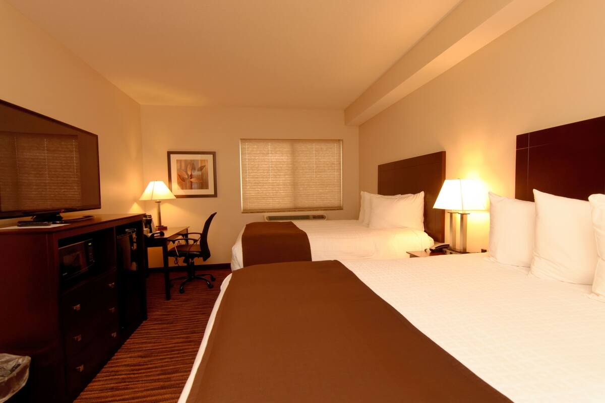 A hotel room with two beds, a desk with a chair, a television, and a window with blinds.