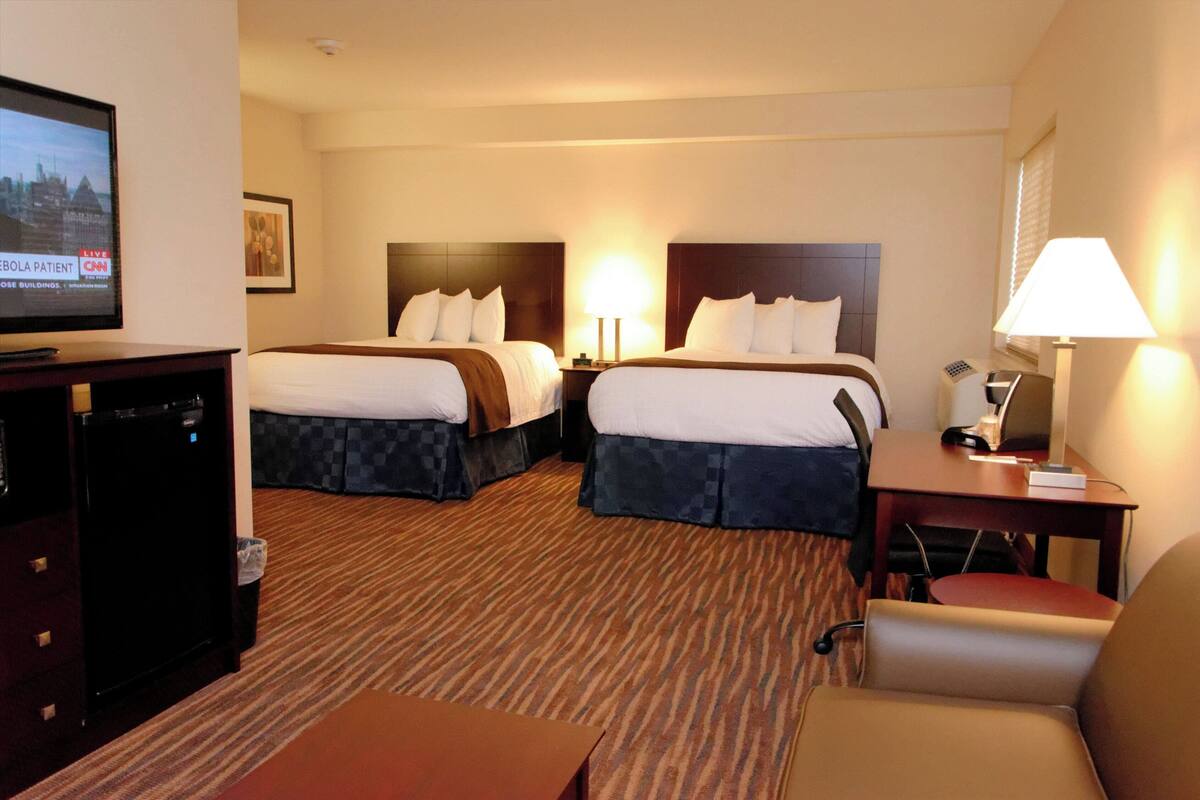 A hotel room with two beds, a television, a desk with a lamp, and a chair.
