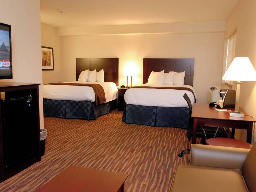 A hotel room with two beds, a television, a desk with a lamp, and a chair.