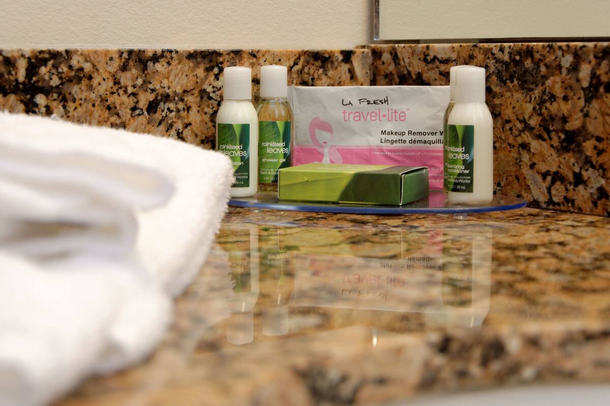 A bathroom counter with toiletries including a green bar of soap, a bottle of lotion, and a makeup remover package.