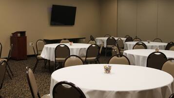 A conference room with multiple round tables, chairs, a podium, and a flat-screen TV on the wall.