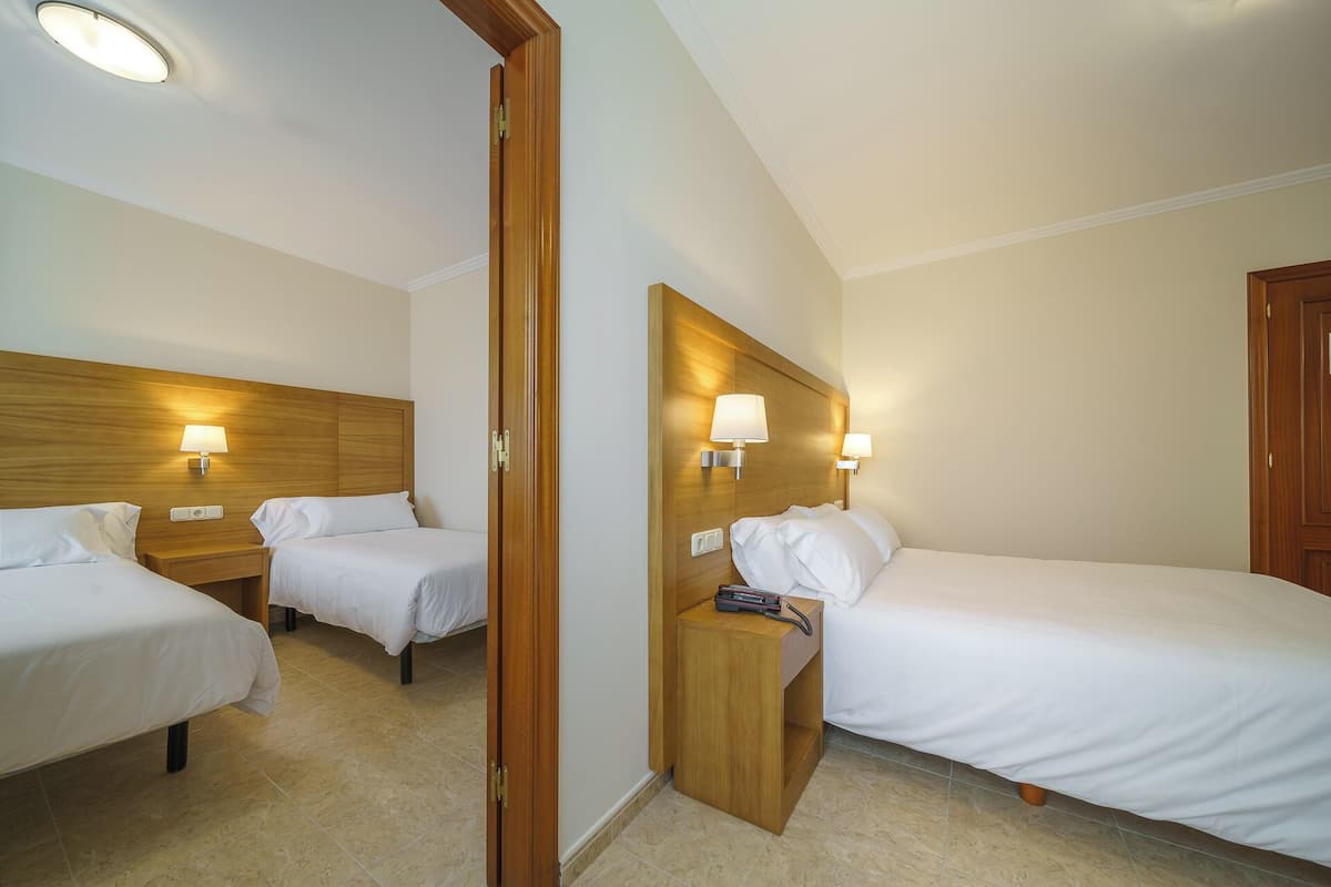 A hotel room with two single beds, wooden headboards, bedside lamps, and a wooden nightstand with a telephone.
