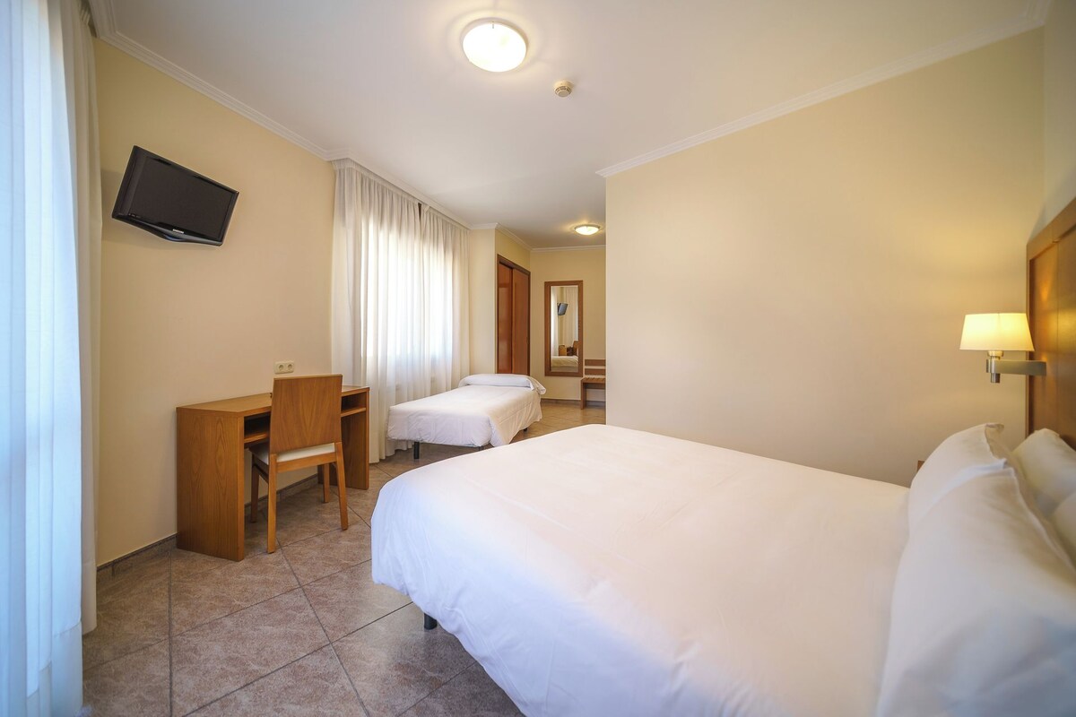 Een hotelkamer met twee eenpersoonsbedden, een bureau met stoel, een flatscreen televisie aan de muur en een bedlampje.