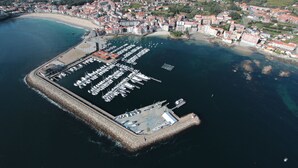 An aerial view of a marina with numerous boats docked, surrounded by a coastal town with red-roofed buildings. - Hotel El Puente (Sanxenxo)