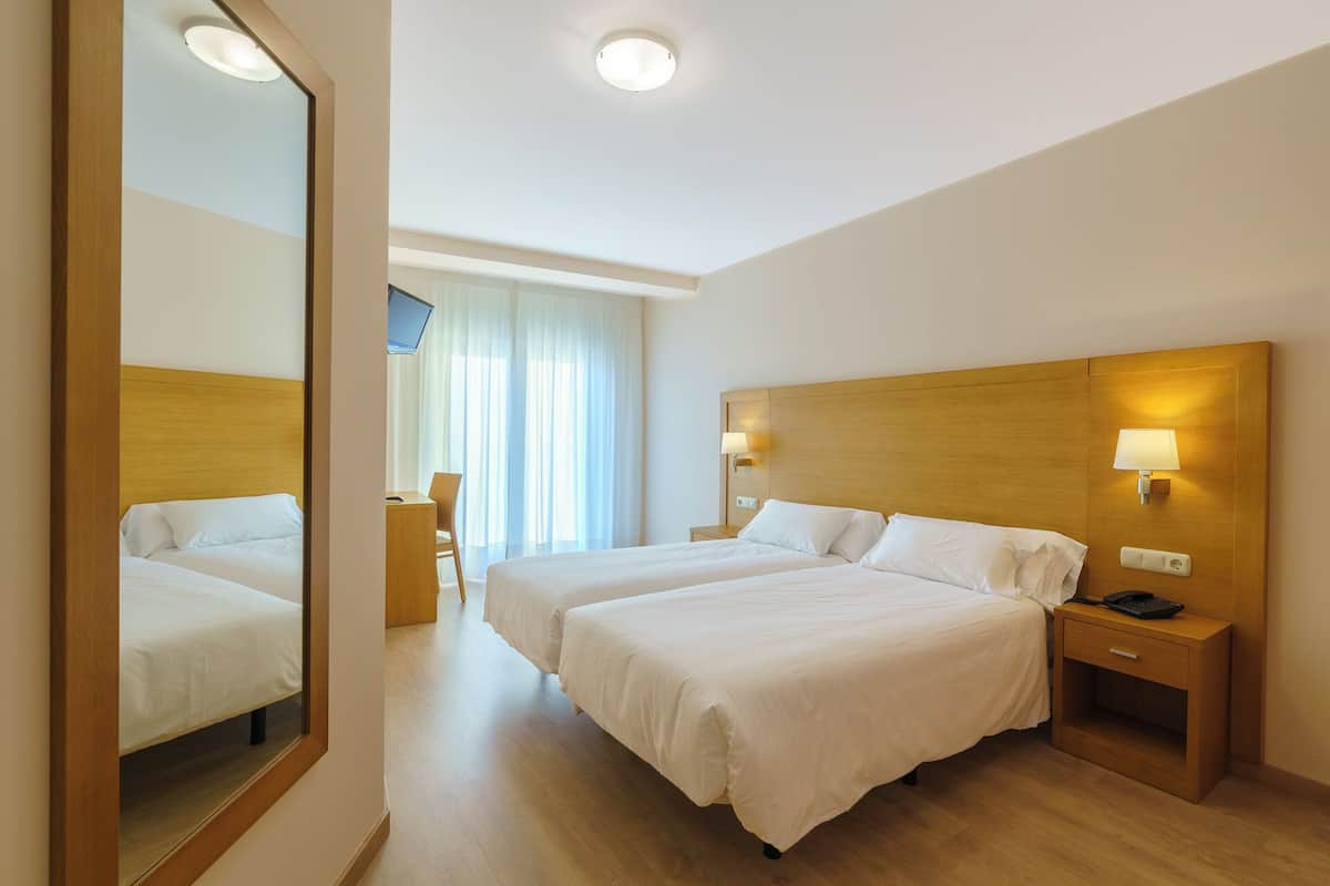 A hotel room with two beds, a desk, a chair, a TV, and a mirror.