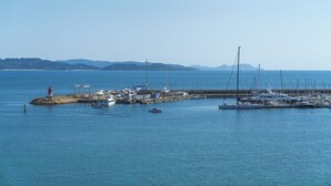 A marina with boats docked, a lighthouse, and a clear view of the water and distant hills. - Hotel El Puente (Sanxenxo)