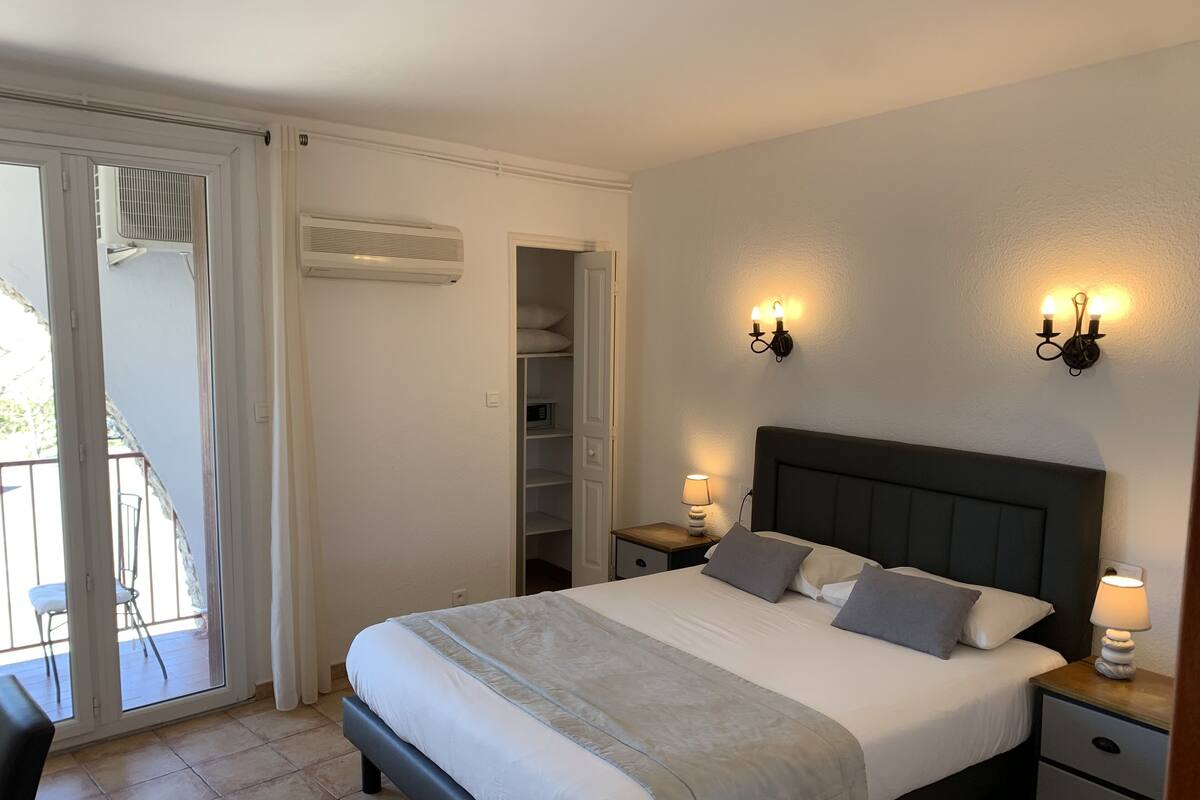 Une chambre à coucher comprenant un lit, des tables de chevet, une armoire et une porte-fenêtre coulissante donnant sur un espace extérieur.