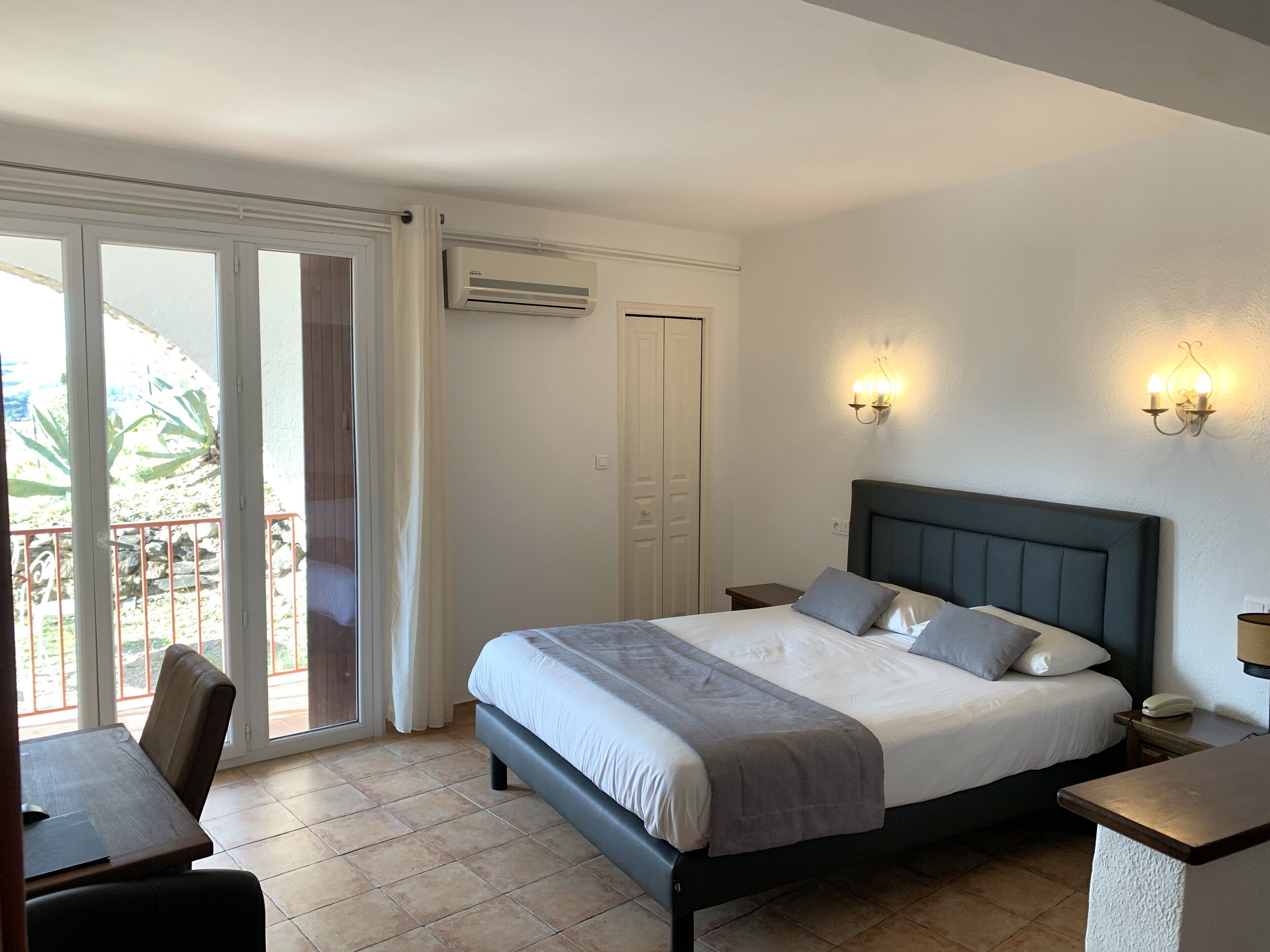 Une chambre à coucher comprenant un lit, des tables de chevet, un bureau et une porte-fenêtre coulissante donnant sur un espace extérieur.