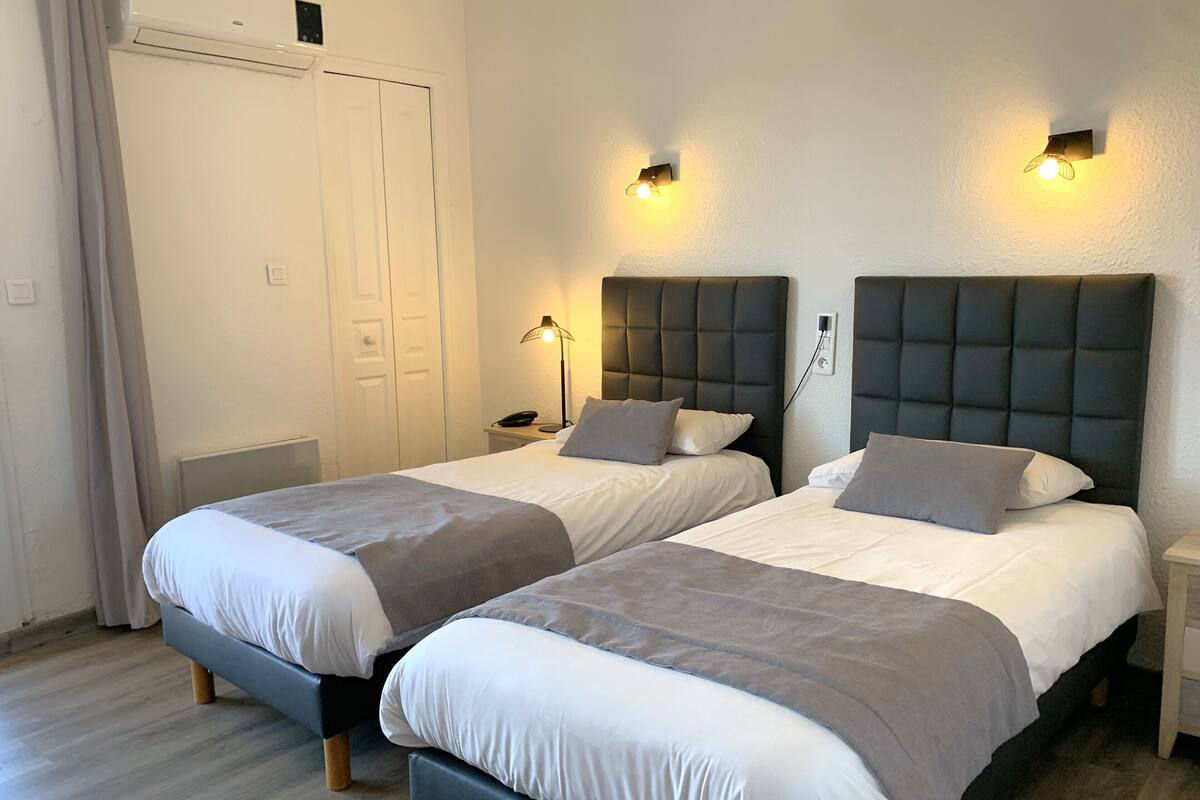 Une chambre double avec deux lits, chacun doté d’une tête de lit, de tables de chevet et de lampes.