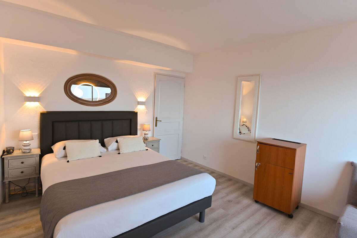 Une chambre bien rangée, avec un lit, des tables de chevet, une armoire et des luminaires fixés au mur.