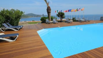 A poolside area with lounge chairs, a wooden deck, and flags of various countries.