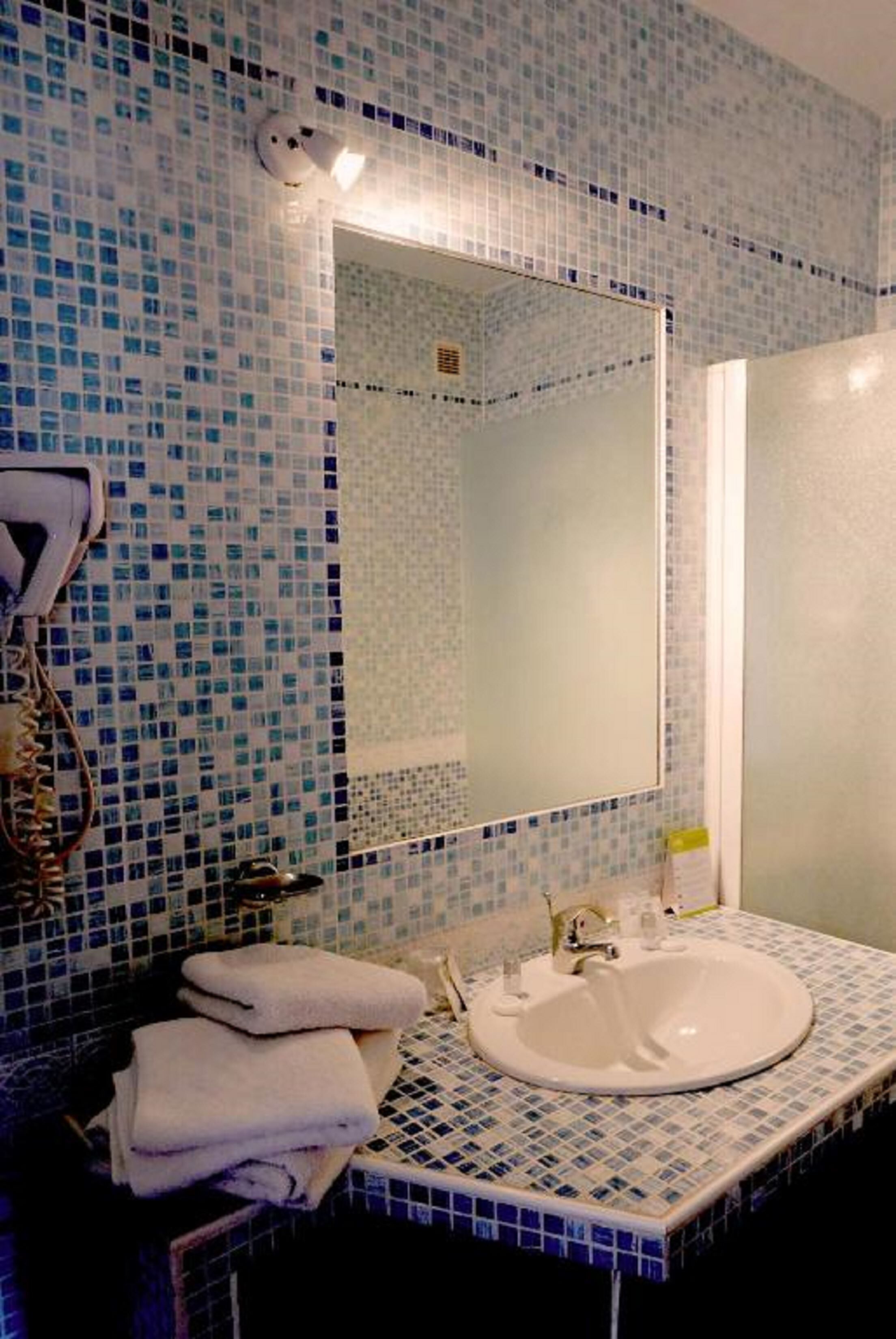 Un baño con pared de azulejos, un lavamanos y un espejo.