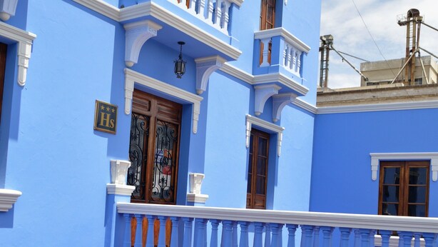 A blue building with a balcony, wooden doors, and potted plants. - Las Mercedes Hostal Residencial (Arequipa)