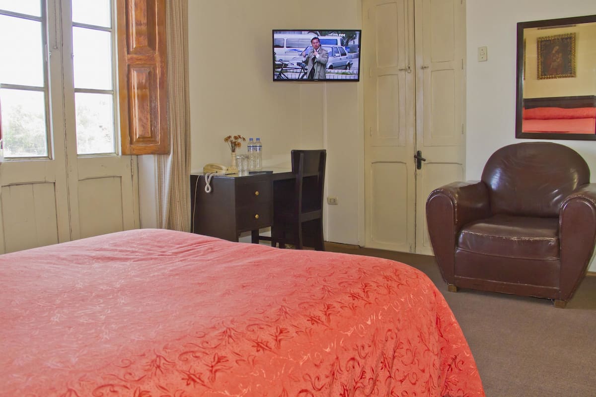 Una habitación de hotel con una cama grande, un escritorio, un sillón de cuero, un televisor y una puerta.