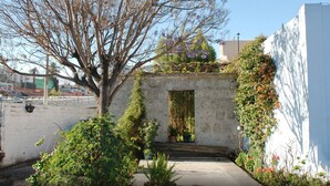 A narrow pathway leading to a small, rustic building with a stone wall, a wooden door, and a tree with bare branches. - Las Mercedes Hostal Residencial (Arequipa)