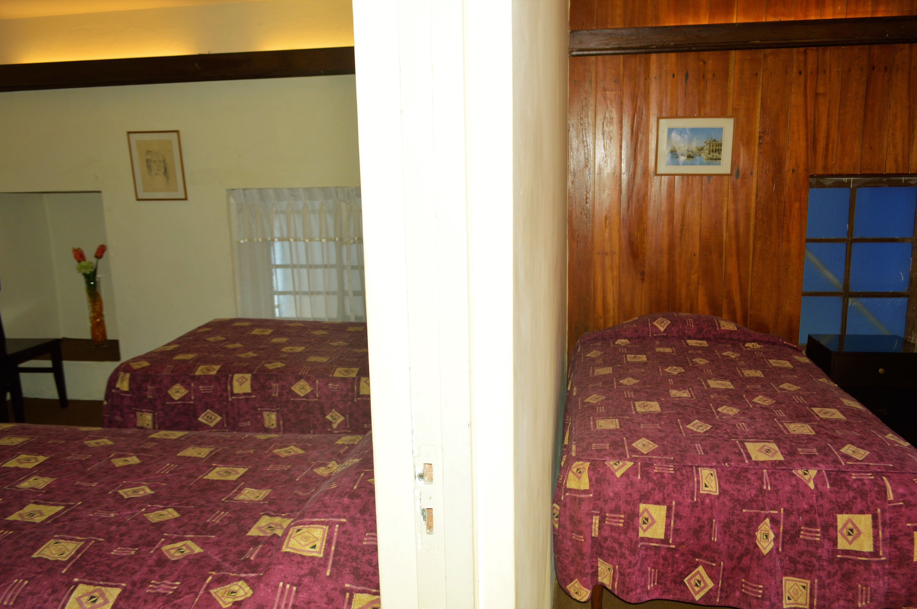 A room with two beds, a wooden wall, a window, and a picture.