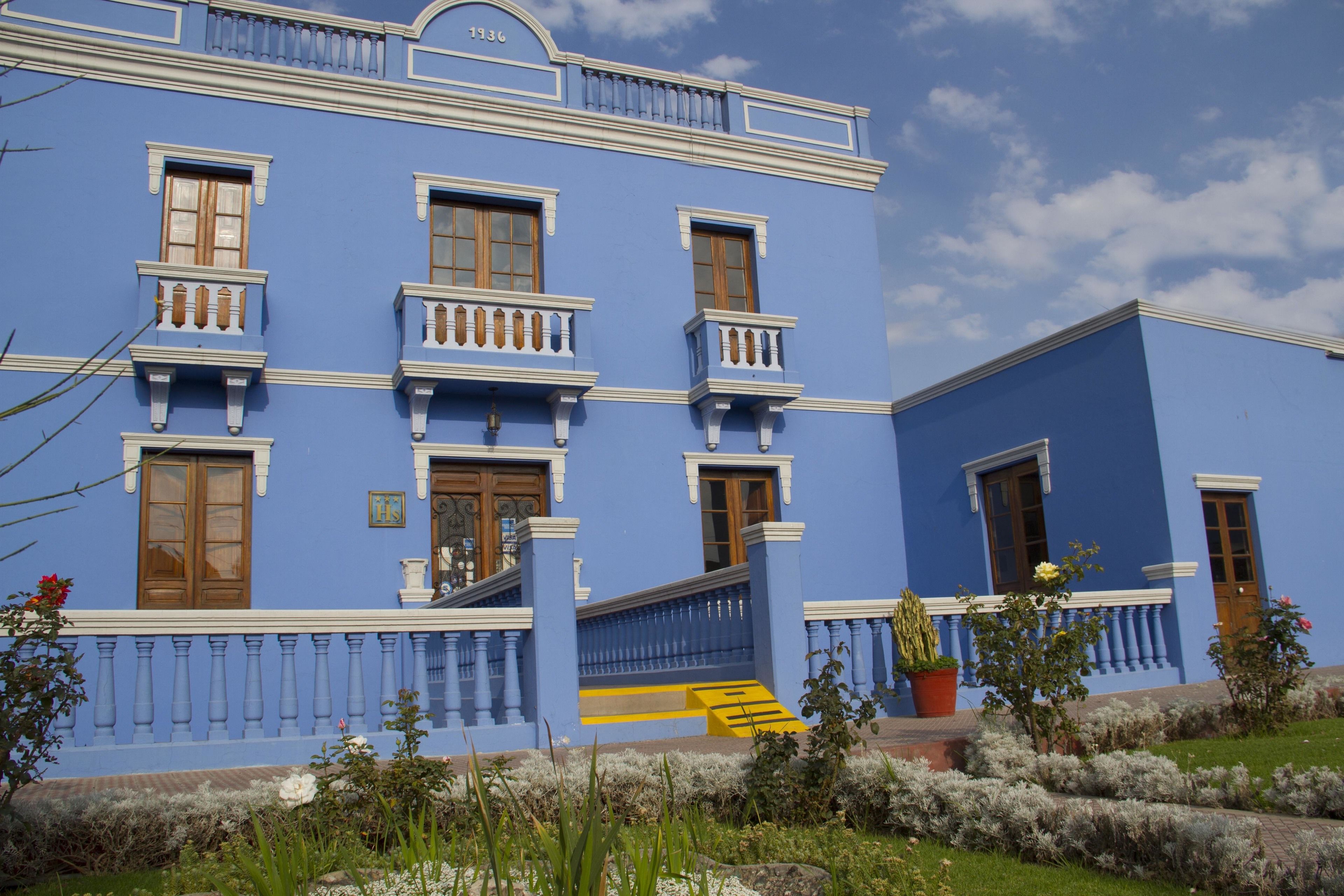 A blue building with multiple windows and balconies, a staircase, and a garden area with plants and flowers.