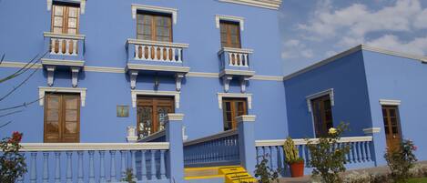 A blue building with multiple windows and balconies, a staircase, and a garden area with plants and flowers.