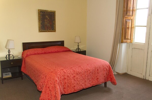 A bedroom with a large bed, two bedside tables with lamps, a framed picture on the wall, and a window with curtains.