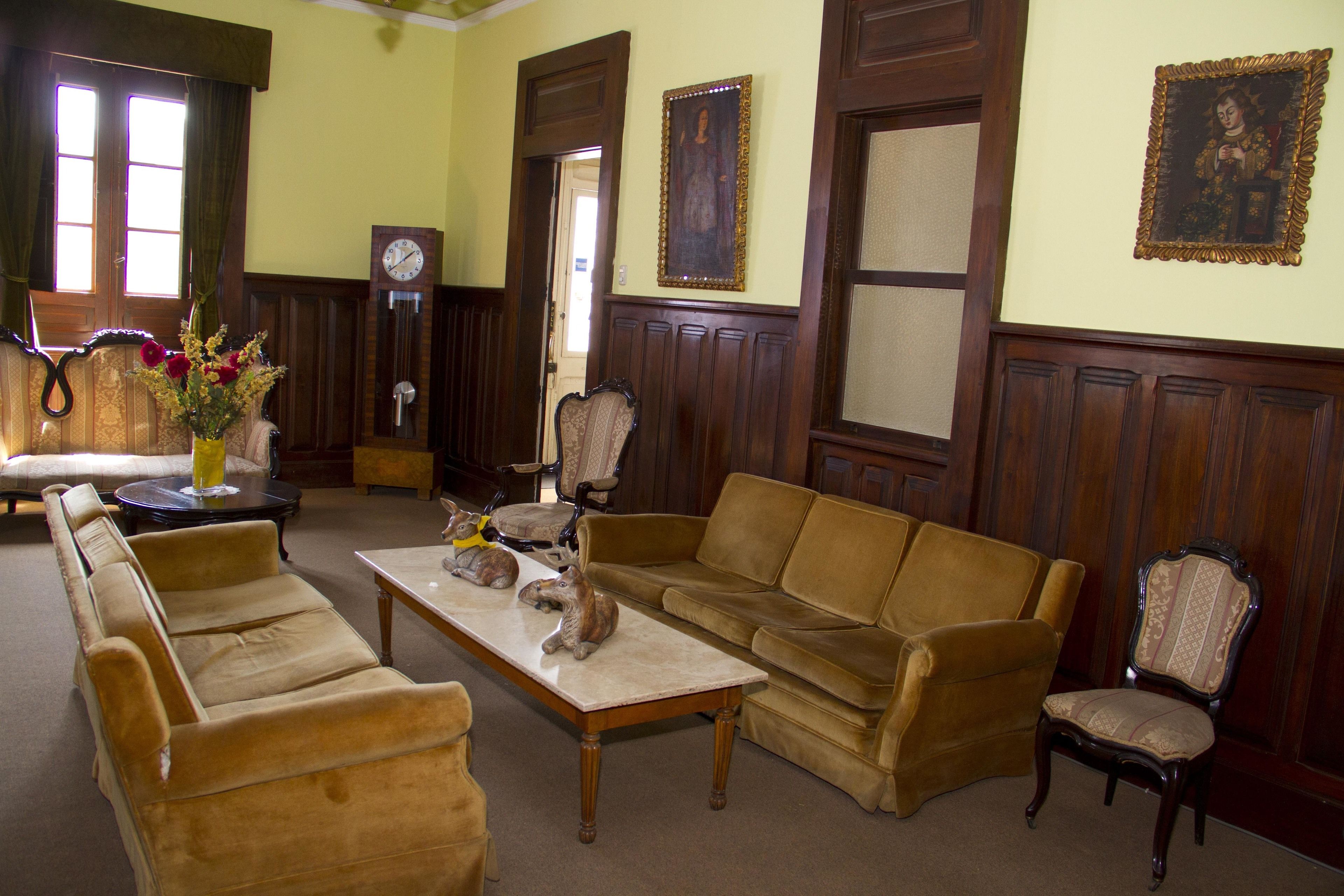 A room with a sofa set, a coffee table, and a chair. There is a clock on the wall and a vase with flowers on the table.