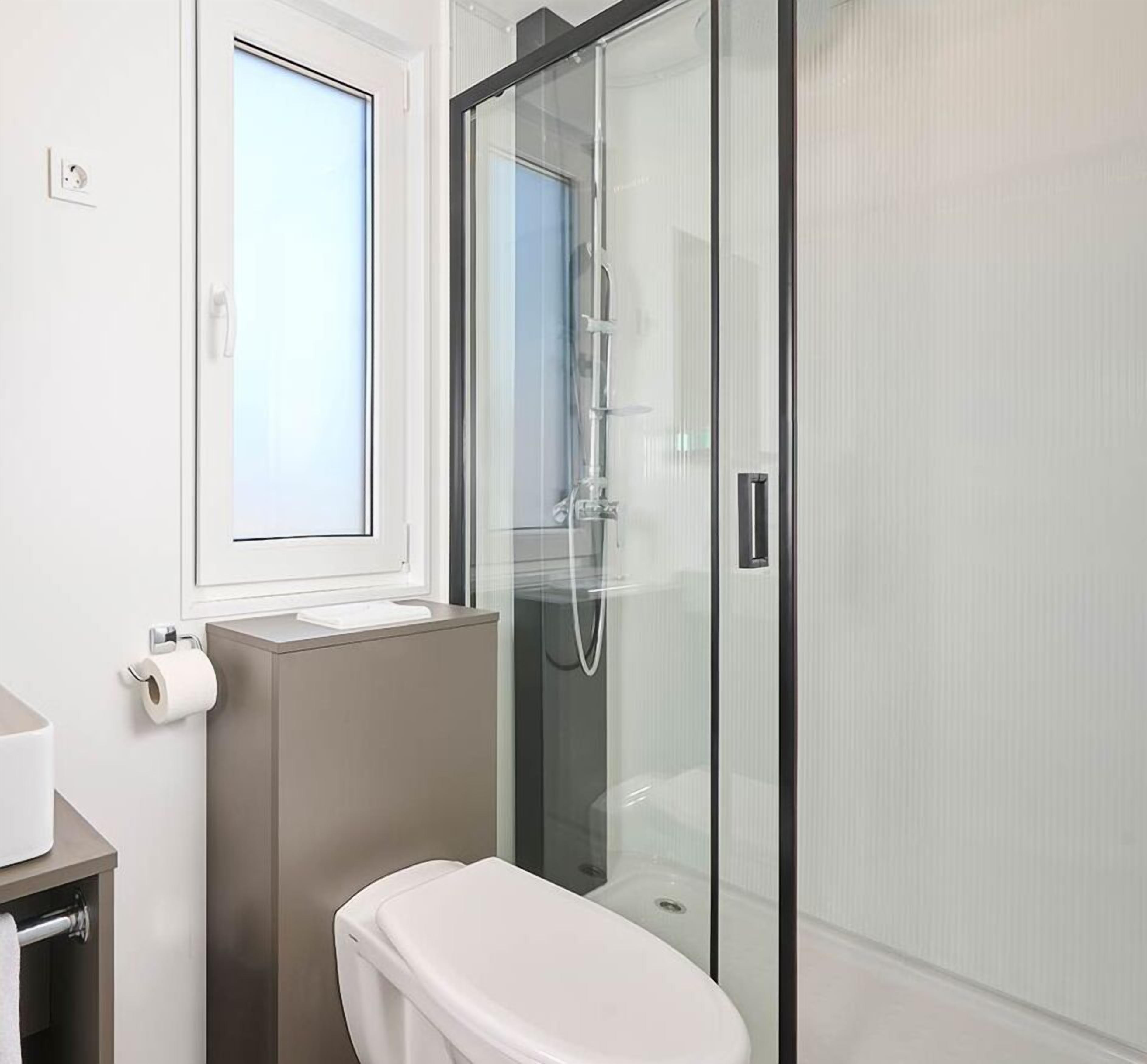 A modern bathroom with a toilet, a shower enclosure, and a window.