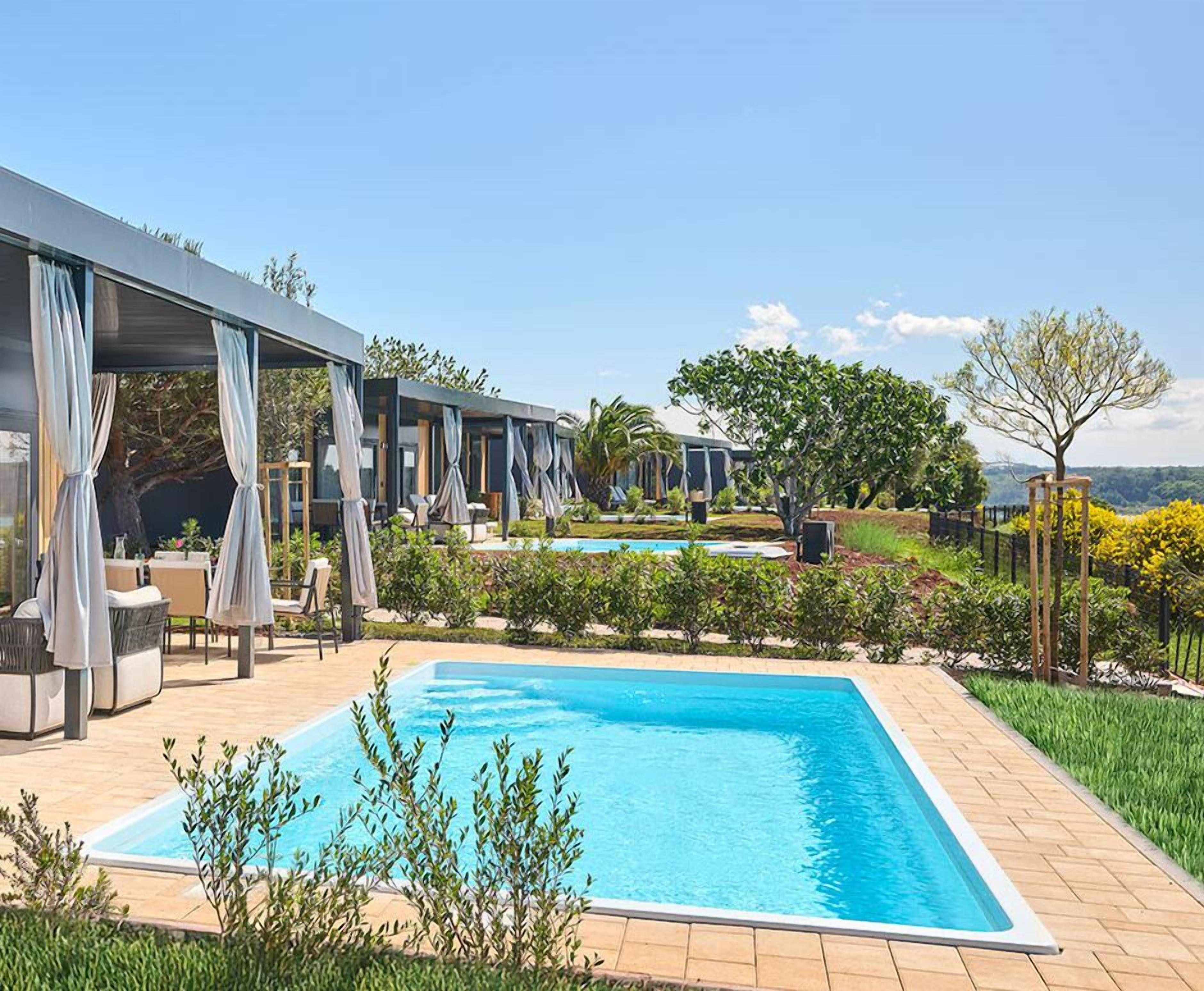 A swimming pool with a covered seating area, a view of the landscape, and a vineyard in the background.