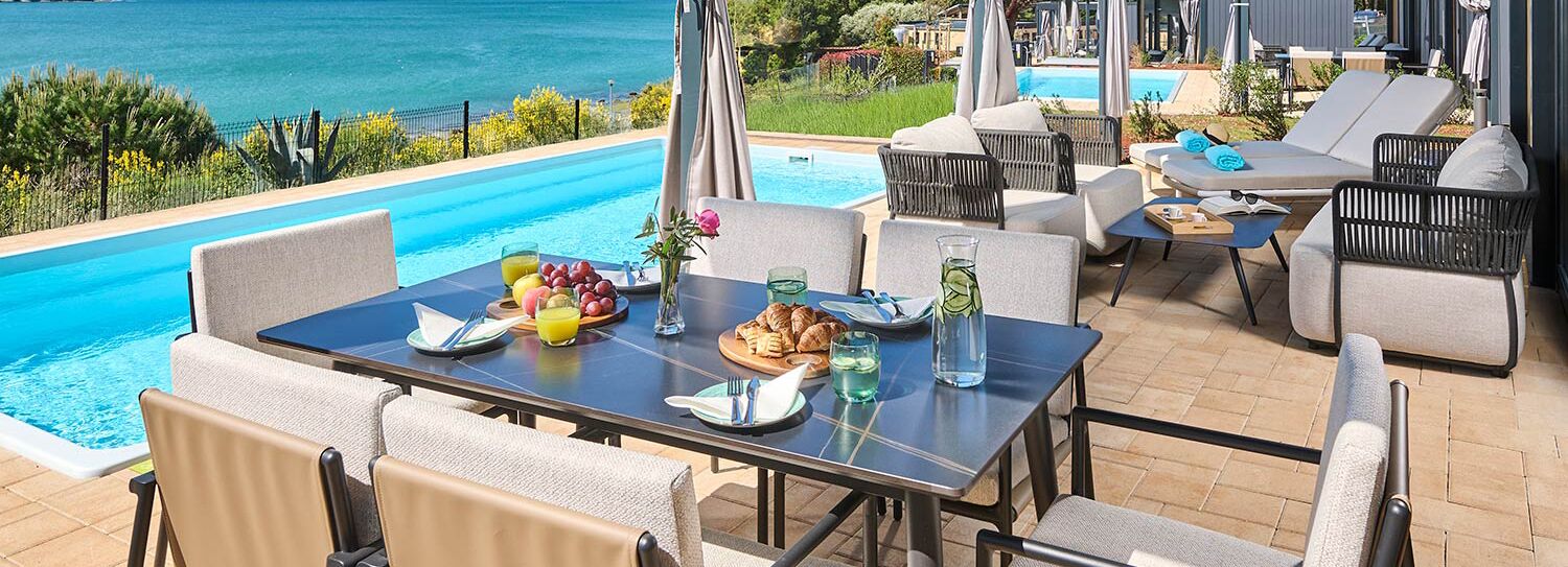 A poolside dining area with a table set for breakfast, overlooking a swimming pool and the sea.