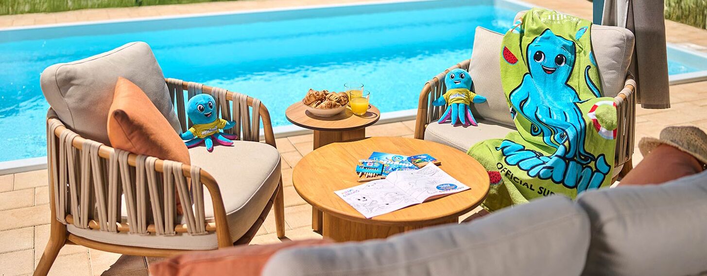 A poolside area with wicker chairs, a table with snacks and drinks, and plush toys.