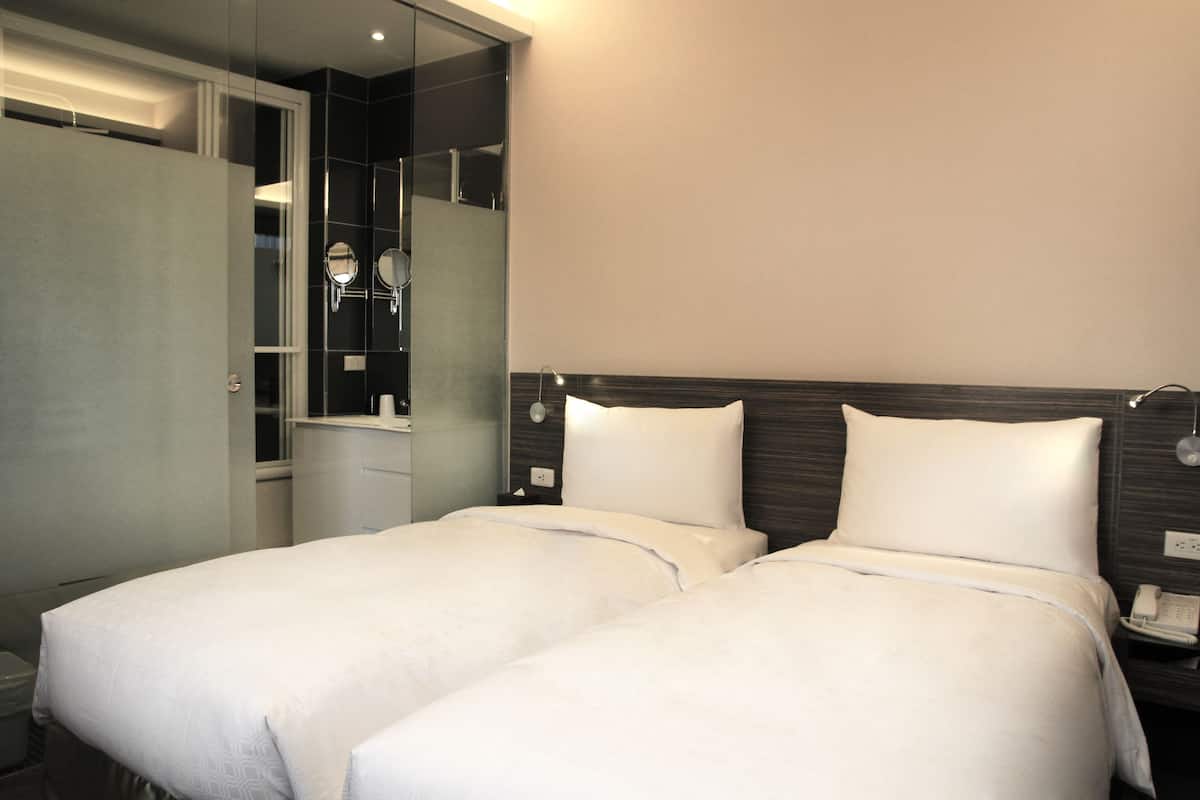 A hotel room with two beds, a wardrobe, a mirror, and a bedside telephone.